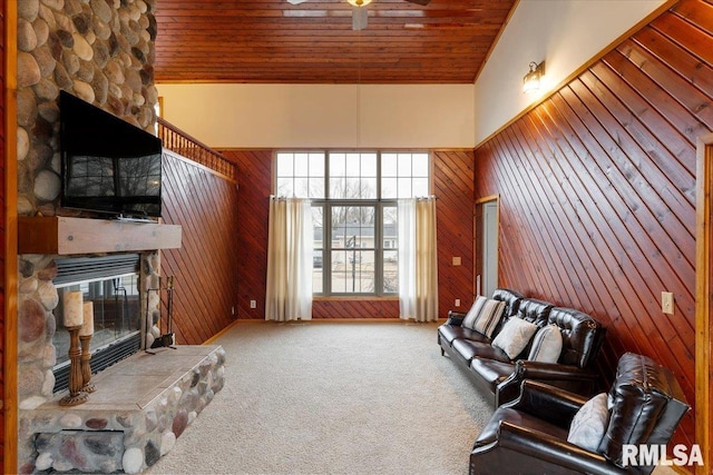 living room with a stone fireplace, wooden ceiling, carpet, and wood walls