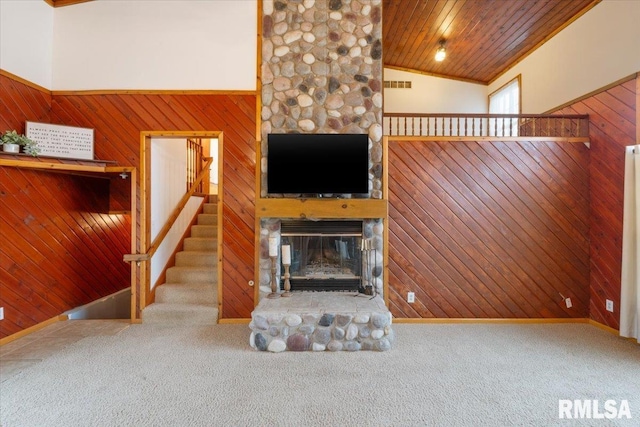 unfurnished living room with a stone fireplace, carpet floors, and wood walls