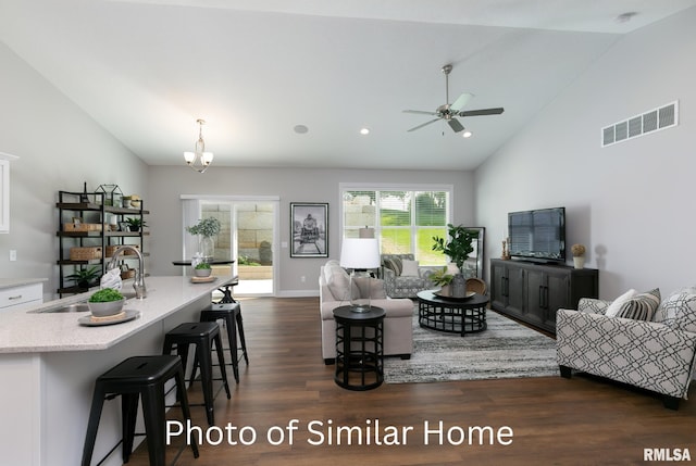 living room with dark wood-type flooring, high vaulted ceiling, ceiling fan with notable chandelier, and sink