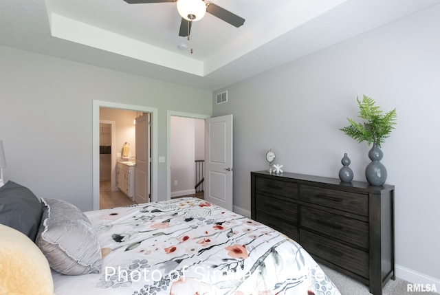 bedroom with ceiling fan, ensuite bathroom, and a raised ceiling