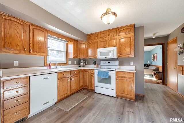 kitchen featuring white appliances, sink, a textured ceiling, and light wood-type flooring