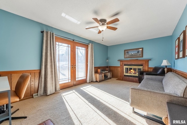 carpeted living room featuring ceiling fan, french doors, a textured ceiling, and wood walls