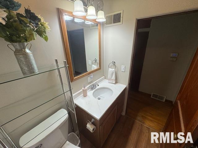 bathroom with vanity, wood-type flooring, a notable chandelier, and toilet