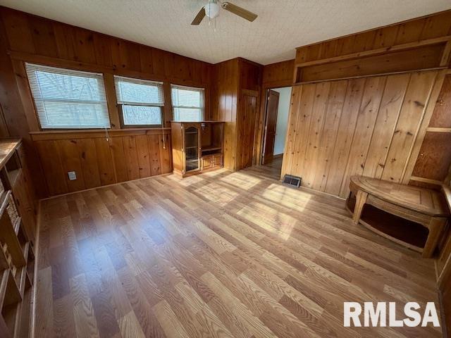 interior space with ceiling fan, wooden walls, light hardwood / wood-style floors, and a textured ceiling