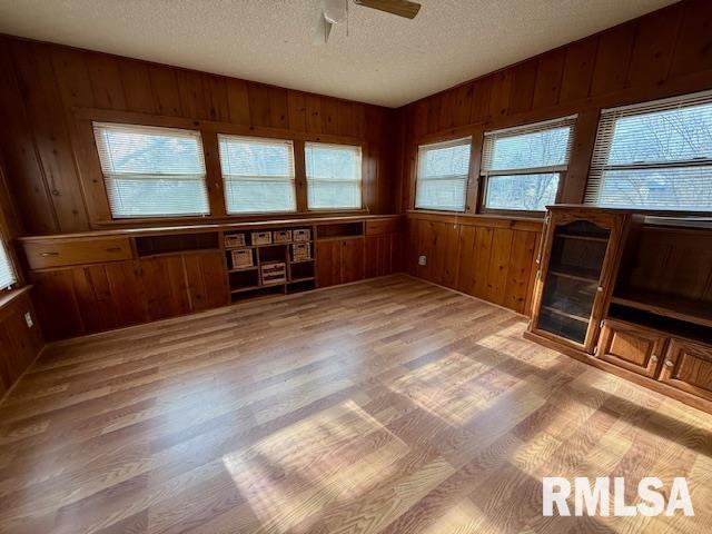 interior space with lofted ceiling, light hardwood / wood-style flooring, wooden walls, and a textured ceiling