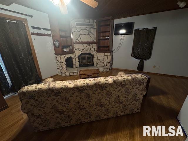 living area with ceiling fan, a stone fireplace, and wood finished floors