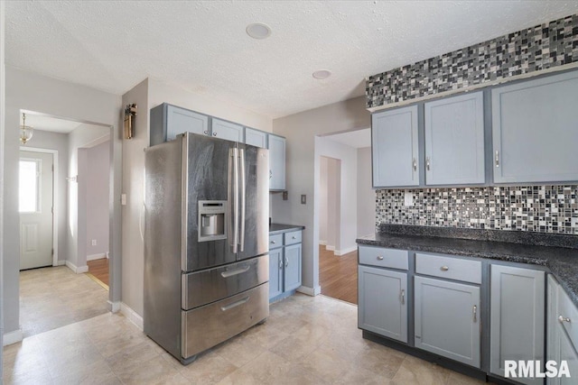 kitchen with gray cabinetry, backsplash, stainless steel fridge, and a textured ceiling