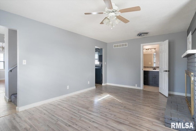 interior space featuring ensuite bath, a fireplace, light hardwood / wood-style floors, and ceiling fan