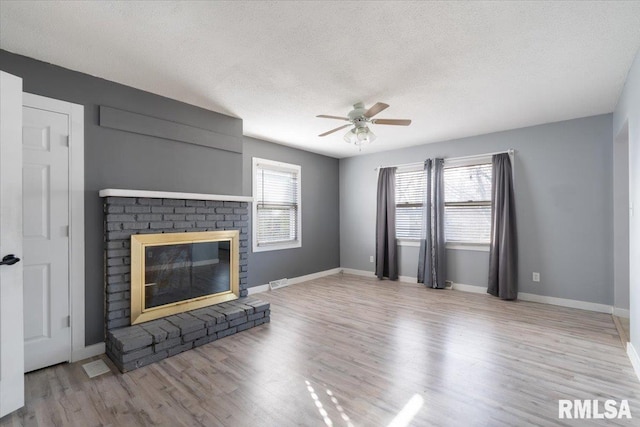 unfurnished living room with ceiling fan, a brick fireplace, light hardwood / wood-style flooring, and a textured ceiling