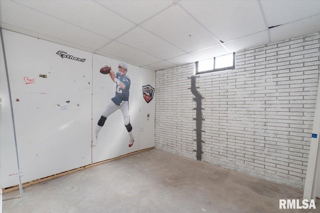 basement featuring a paneled ceiling and brick wall