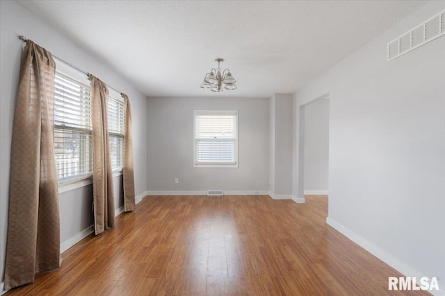 unfurnished room featuring an inviting chandelier and light hardwood / wood-style flooring