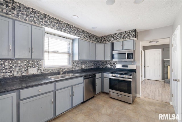 kitchen featuring tasteful backsplash, sink, gray cabinetry, stainless steel appliances, and a textured ceiling