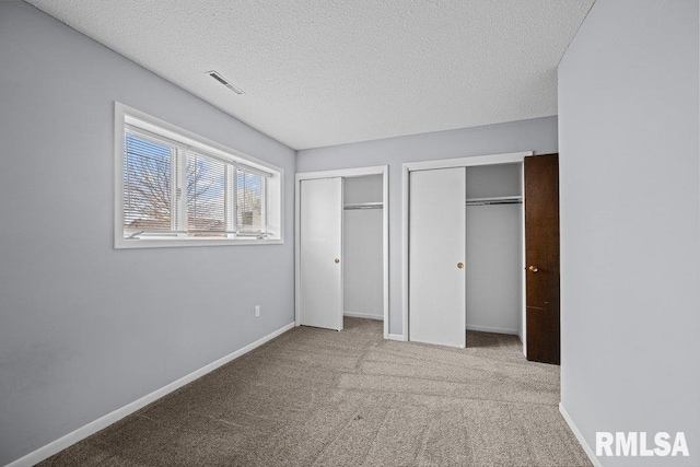 unfurnished bedroom with two closets, a textured ceiling, and carpet flooring