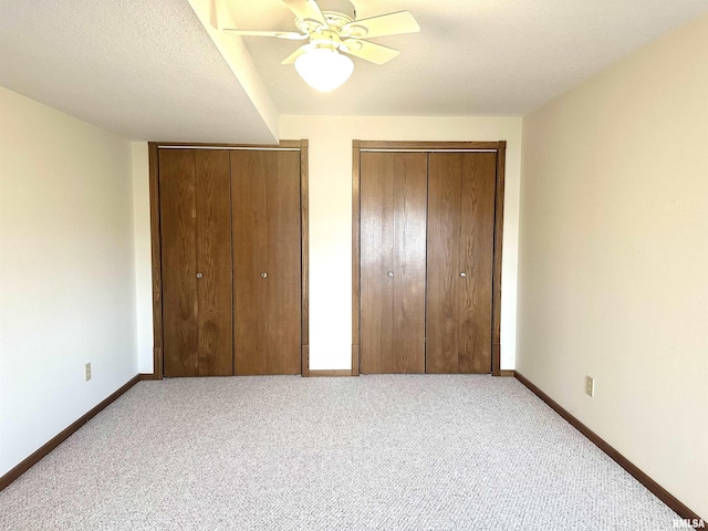 unfurnished bedroom with ceiling fan, a textured ceiling, light colored carpet, and multiple closets