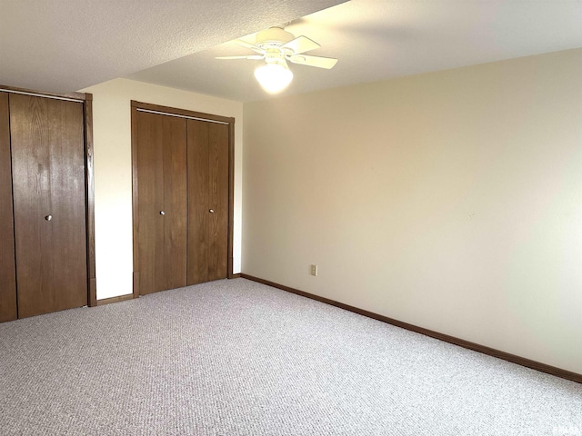 unfurnished bedroom featuring multiple closets, light colored carpet, a textured ceiling, and ceiling fan