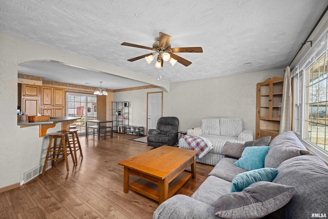 living room with hardwood / wood-style flooring, ceiling fan with notable chandelier, and a textured ceiling