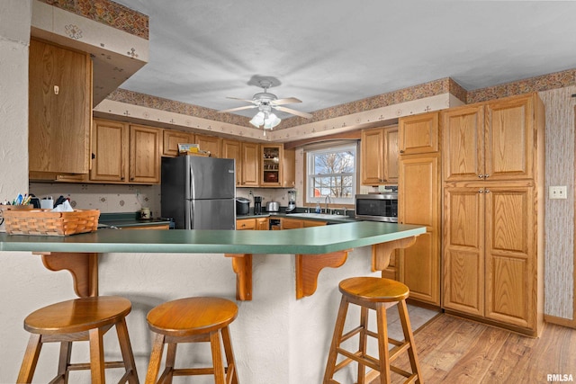 kitchen featuring sink, a breakfast bar area, appliances with stainless steel finishes, ceiling fan, and light hardwood / wood-style floors