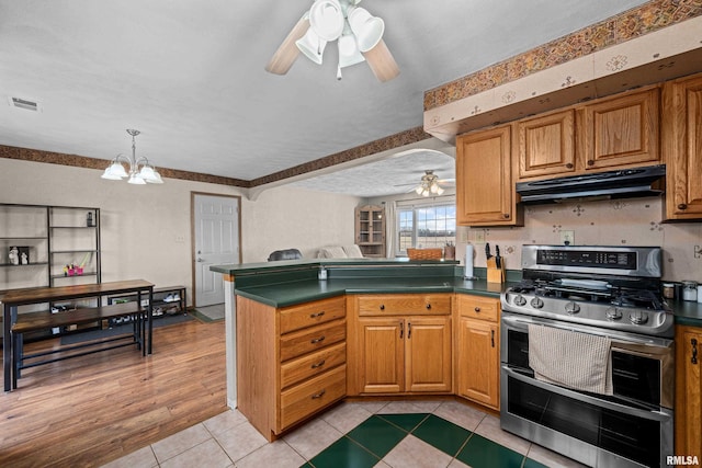 kitchen with double oven range, light tile patterned flooring, ceiling fan with notable chandelier, decorative light fixtures, and kitchen peninsula