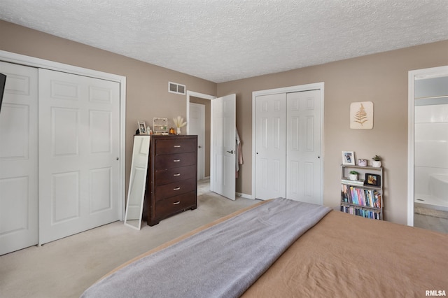 carpeted bedroom with a textured ceiling, ensuite bath, and multiple closets