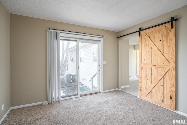 empty room with a barn door, carpet floors, and a textured ceiling