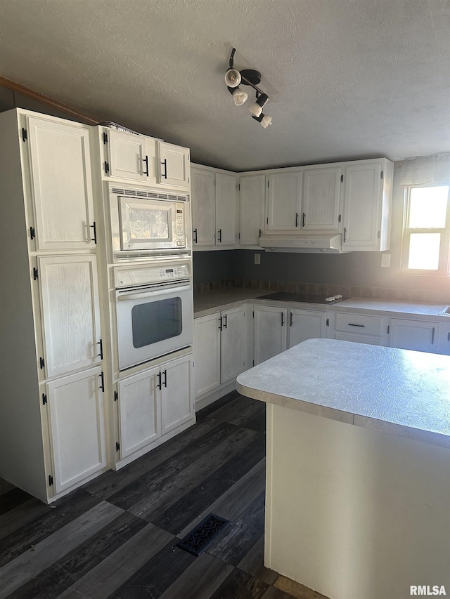 kitchen with dark wood-type flooring, a textured ceiling, white cabinets, and white appliances