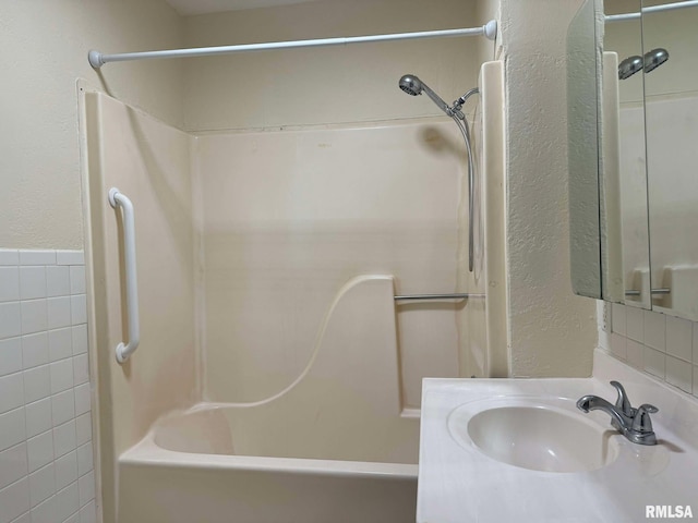 bathroom with washtub / shower combination, vanity, and tile walls