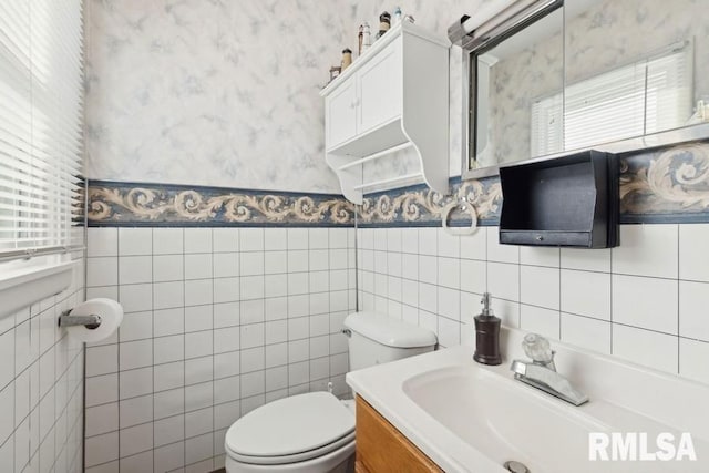 half bath with wallpapered walls, toilet, vanity, and a wealth of natural light