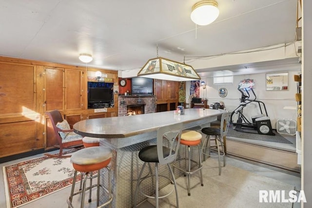 kitchen featuring brown cabinetry, a breakfast bar area, a fireplace, and concrete floors