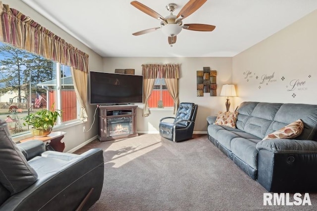 carpeted living room featuring baseboards, a ceiling fan, and a glass covered fireplace