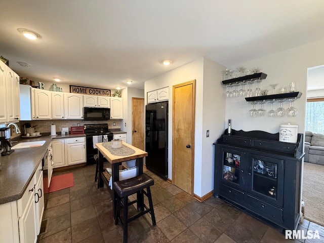 kitchen featuring black appliances, a sink, tasteful backsplash, dark countertops, and white cabinets