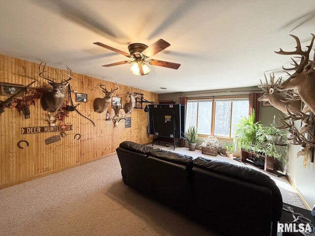 living area featuring ceiling fan, wood walls, and carpet flooring