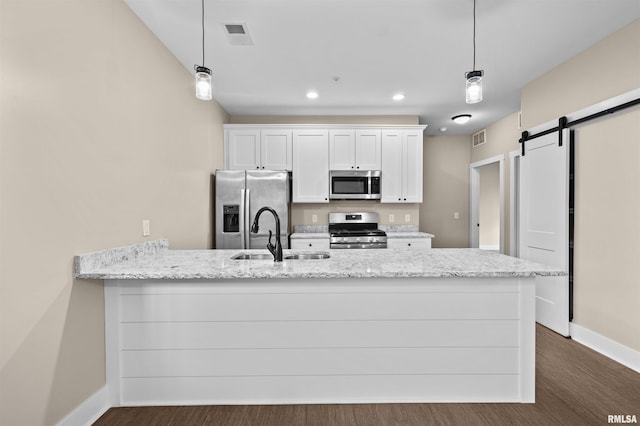 kitchen with pendant lighting, sink, stainless steel appliances, white cabinets, and a barn door