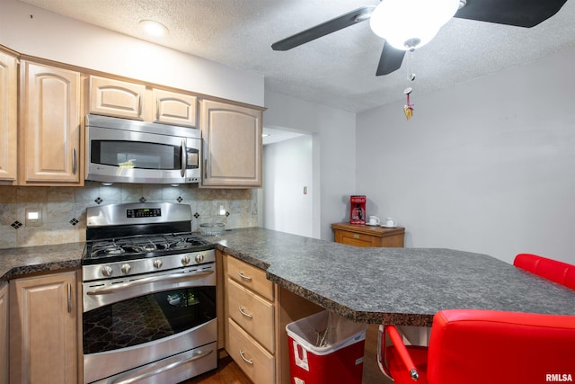 kitchen with dark countertops, backsplash, appliances with stainless steel finishes, a textured ceiling, and a peninsula