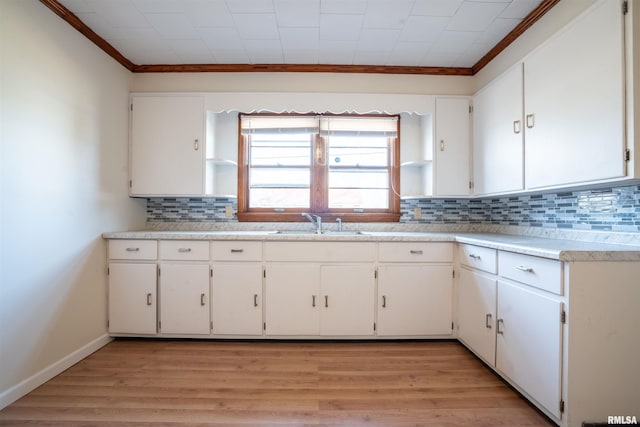 kitchen featuring sink, tasteful backsplash, crown molding, light hardwood / wood-style floors, and white cabinets