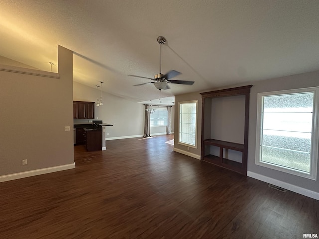 unfurnished living room featuring lofted ceiling, dark hardwood / wood-style flooring, ceiling fan with notable chandelier, and a wealth of natural light