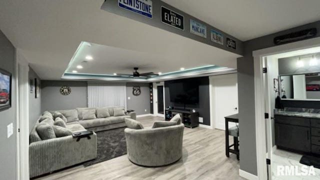 home theater featuring a raised ceiling, ceiling fan, and light hardwood / wood-style floors