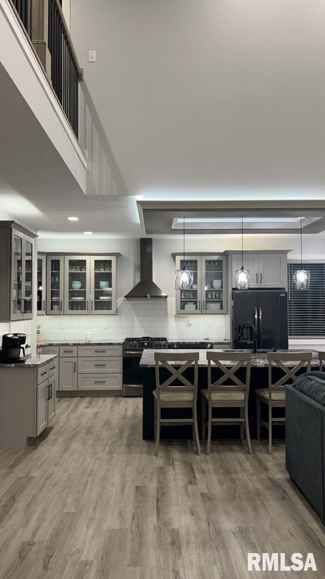 kitchen featuring gray cabinets, stainless steel range with gas stovetop, light stone countertops, black fridge, and wall chimney exhaust hood