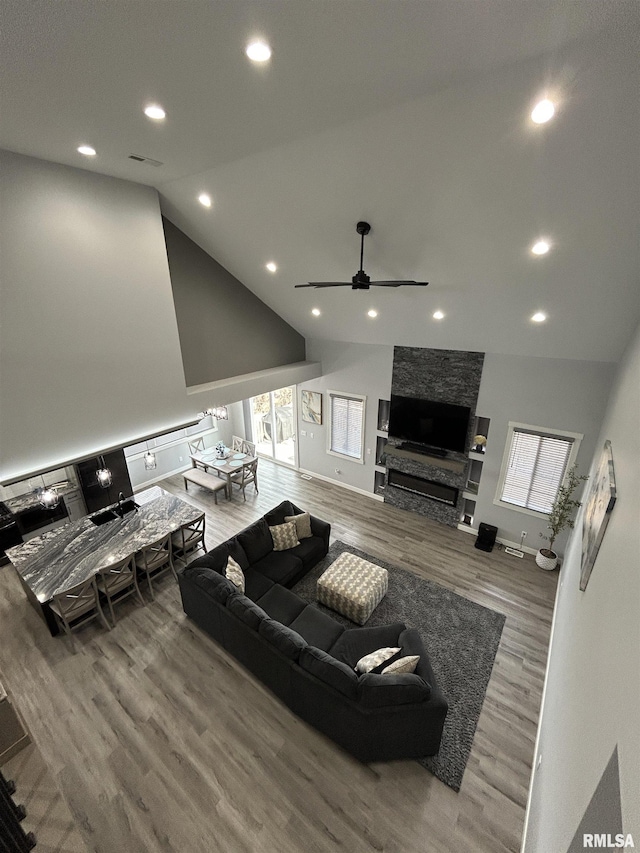 living room featuring ceiling fan, wood-type flooring, a fireplace, and high vaulted ceiling