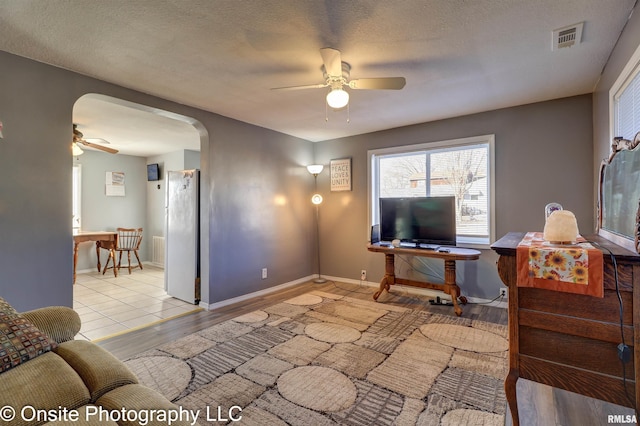 living room with a textured ceiling, ceiling fan, and light hardwood / wood-style floors