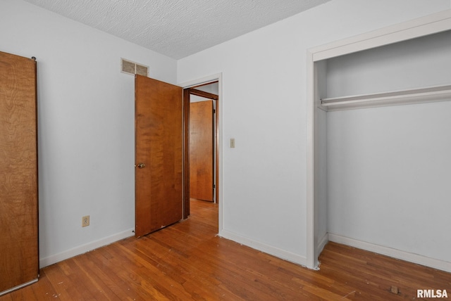 unfurnished bedroom featuring hardwood / wood-style floors, a textured ceiling, and a closet