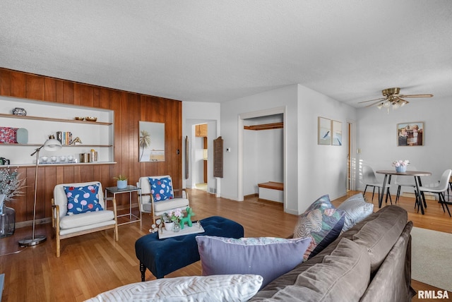 living room with hardwood / wood-style flooring, built in features, ceiling fan, a textured ceiling, and wood walls