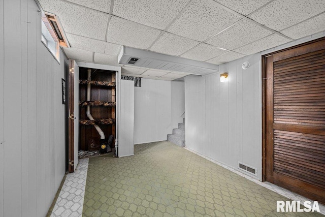 basement featuring a drop ceiling and wooden walls