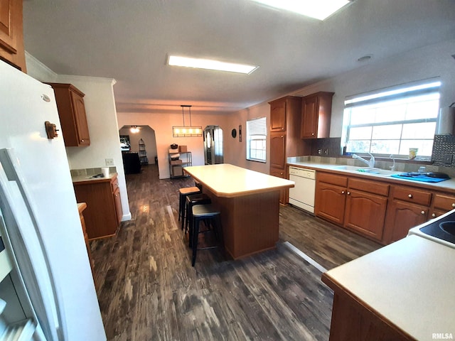 kitchen with pendant lighting, sink, dark wood-type flooring, white dishwasher, and a kitchen island