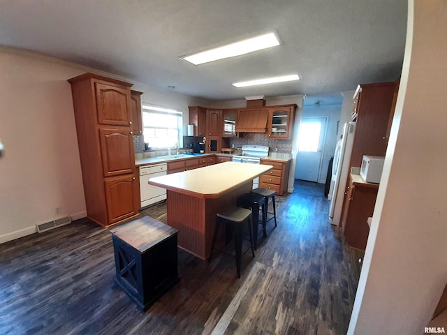 kitchen featuring dark hardwood / wood-style flooring, a center island, a breakfast bar area, and white appliances