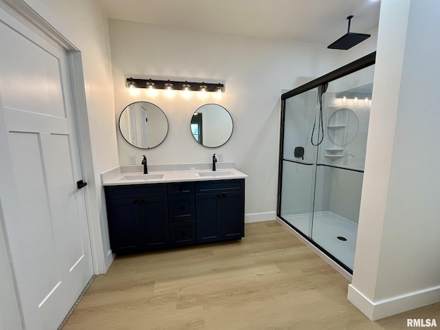 bathroom with a shower stall, wood finished floors, double vanity, and a sink