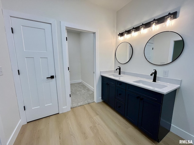 full bath with double vanity, wood finished floors, baseboards, and a sink