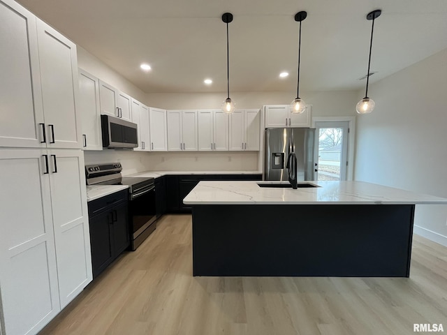 kitchen with light stone countertops, light wood-style flooring, appliances with stainless steel finishes, white cabinets, and a sink