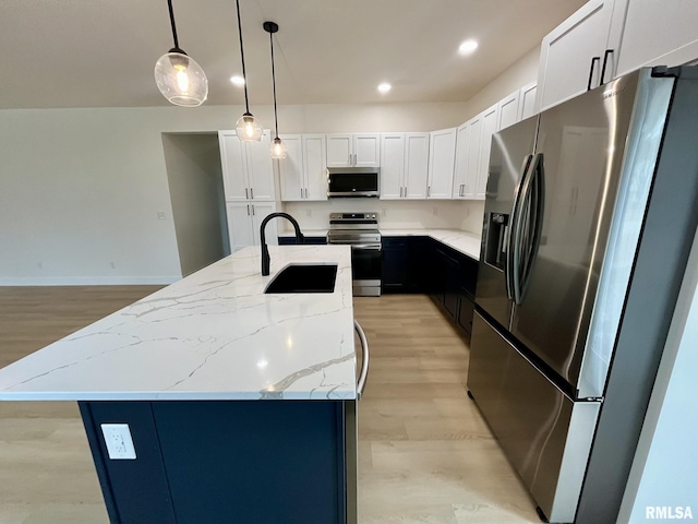 kitchen featuring a kitchen island with sink, a sink, stainless steel appliances, white cabinetry, and light wood-type flooring
