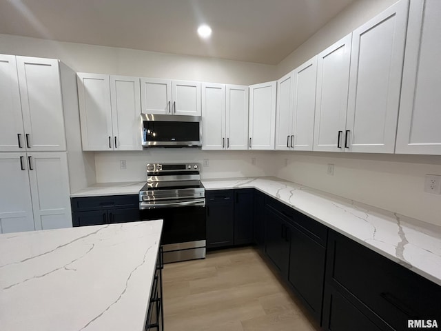 kitchen featuring white cabinets, dark cabinets, light wood finished floors, and stainless steel appliances