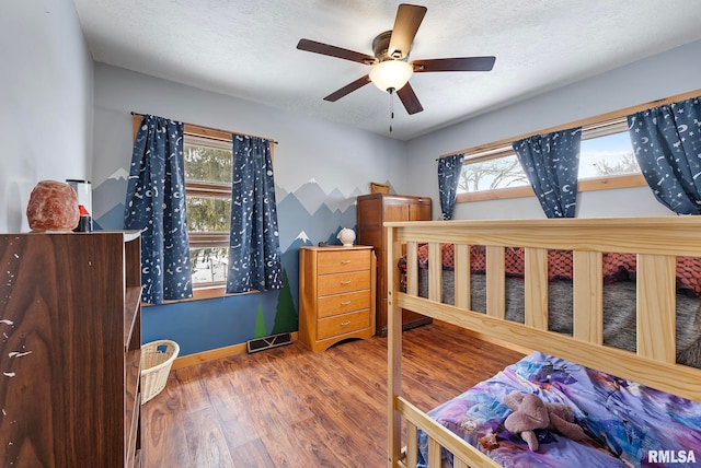 bedroom with a textured ceiling, wood finished floors, a ceiling fan, visible vents, and baseboards